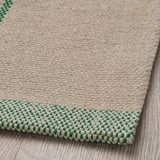 Primo piano di un morbido tappeto di cotone beige con bordo a scacchi verdi, che mostra la sua trama intrecciata.