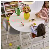 Bambini che giocano a tavola con giocattoli, stanza colorata, pianta, libri.