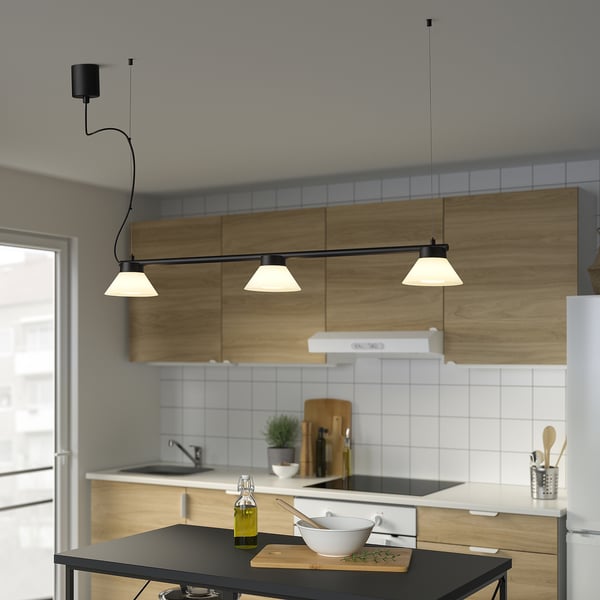Cucina moderna con lampada a sospensione nera SAMBORD sopra l'isola. La lampada ha tre coni. Alzatina bianca, armadi in legno e olio d'oliva sul bancone.