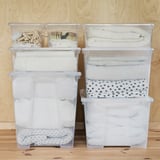 Quattro scatole di plastica SAMLA trasparenti, impilate e organizzate con asciugamani, vestiti e mollette piegati; Ideale per lo stoccaggio e un facile accesso.