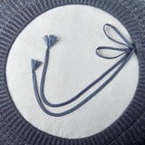 Pouf blu con rivestimento in maglia, caratterizzato da nappine e coulisse per un appeal estetico e funzionale.