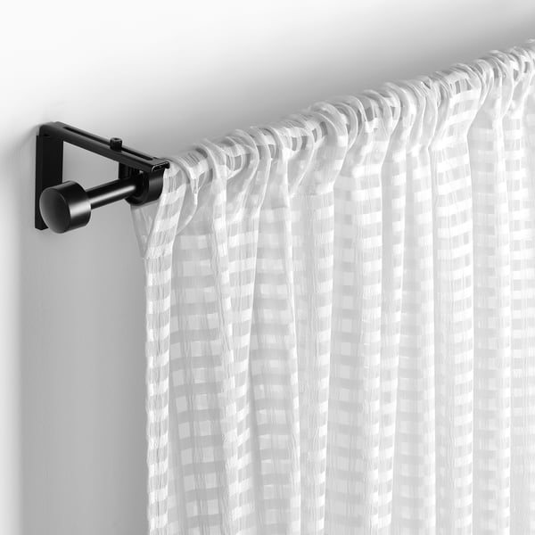 Tende trasparenti bianche con un sottile motivo a quadri sono appese a un'asta nera, garantendo privacy e lasciando passare la luce.