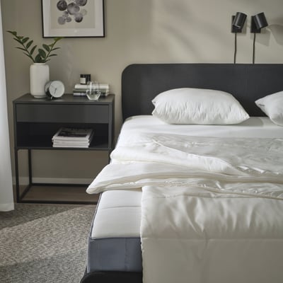 Camera da letto moderna con letto SANDGRÄSMAL, testiera elegante, comodino minimalista.