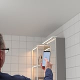 Uomo in bagno che regola le luci sullo smartphone.