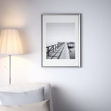 Bianco e nero un molo di legno su un muro. Grande cornice d'argento sopra un letto con una lampada e un cuscino.