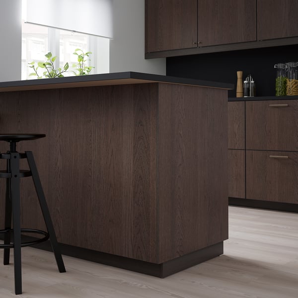 Cucina moderna con armadi SINARP in legno scuro, elegante sgabello da bar e piccola pianta.
