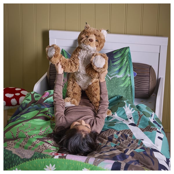 Il bambino si sdraia sul letto abbracciando un grande giocattolo morbido di lince. Il letto ha biancheria da letto colorata e fantasia.