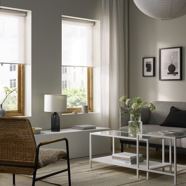Soggiorno moderno con tenda grigia, sedia in vimini e divano grigio. Grandi finestre, piante e opere d'arte alle pareti.