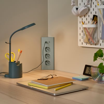 Scrivania in legno con prolunga nera SKOTAT, laptop, quaderni, lampada e pianta. Design minimalista, si fonde con l'arredamento.