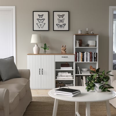 Soggiorno con credenza e libreria SKRUVBY, decorato con piante, libri e opere d'arte delle farfalle, e un accogliente divano.