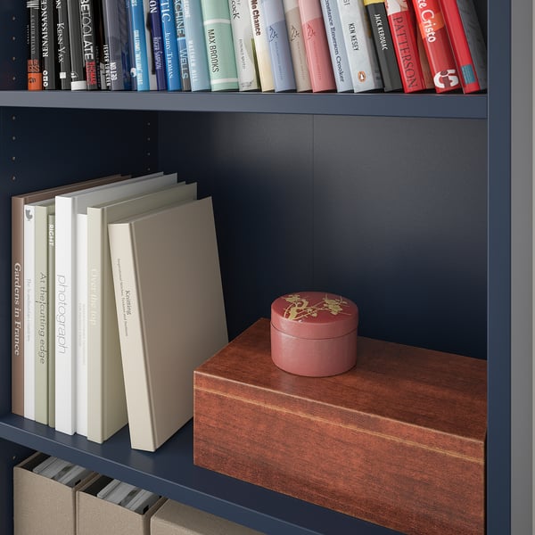 Libreria con ripiani regolabili in blu scuro, che contiene vari libri e una scatola decorativa rossa.