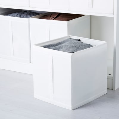 Tre scatole SKUBB bianche in un armadio, che conservano oggetti come coperte, calzini e maglioni. Ogni scatola è dotata di maniglie per un facile accesso.