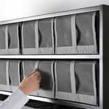 Persona che posiziona scatole di scarpe SKUBB in rete sullo scaffale. Le scatole sono organizzate e l'aria circola attraverso la rete.