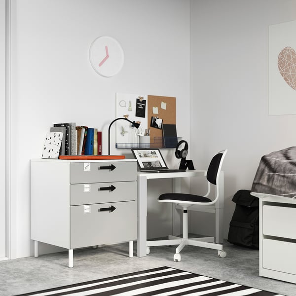 Piccola scrivania bianca, SMÅSTAD, con cassetti grigi nell'angolo della camera da letto. Laptop, libri e sedia posizionati su di esso. Design moderno e minimalista.