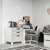 Area studio minimalista per bambini con scrivania e sedia SMÅSTAD bianche, libri, laptop e orologio da parete.