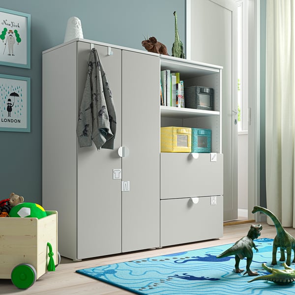 Moderna cameretta per bambini con mobile portaoggetti SMÅSTAD bianco, tappeto blu, dinosauri giocattolo e decorazioni colorate.
