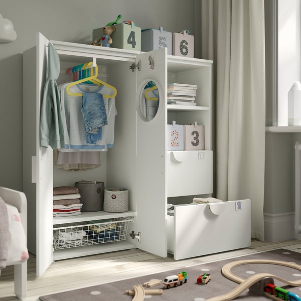 Armadio bianco per bambini con anta aperta, vestiti, mensole, giocattoli e cassetti.