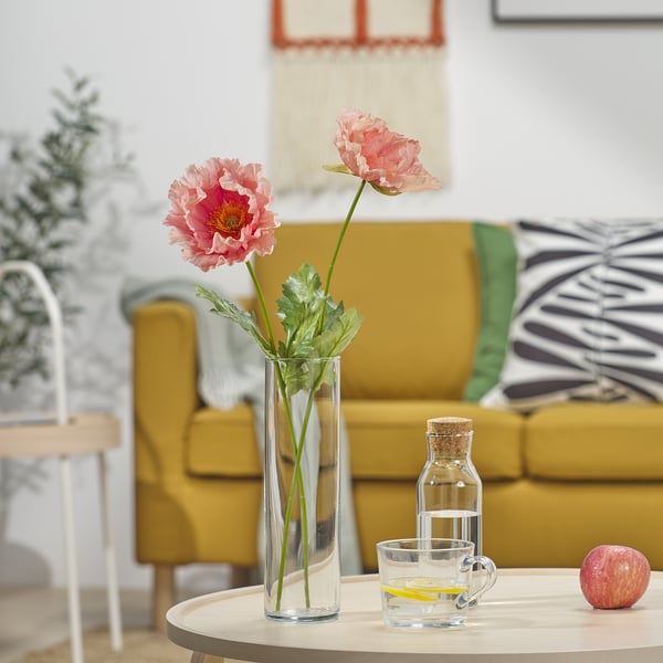 Divano giallo con cuscini bianchi e neri, tavolino rotondo con fiori rosa, tazza di vetro e mela rossa.
