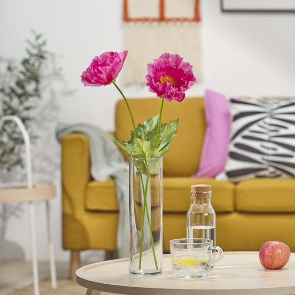Fiori rosa in vaso sul tavolo con tazza e mela, divano giallo.