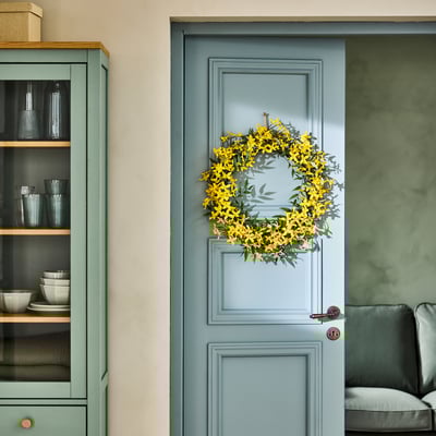 Ghirlanda floreale gialla sulla porta blu pallido, accanto all'armadio verde con piatti.