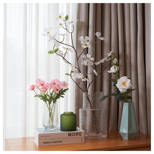 Tre vasi con fiori vicino a una finestra: fiori rosa, candela, bianchi, verde acqua.