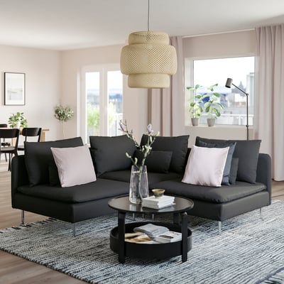 Soggiorno moderno con grande divano componibile nero SÖDERHAMN, elegante tavolino, elegante lampada a sospensione e ampie finestre con vista sulla città.