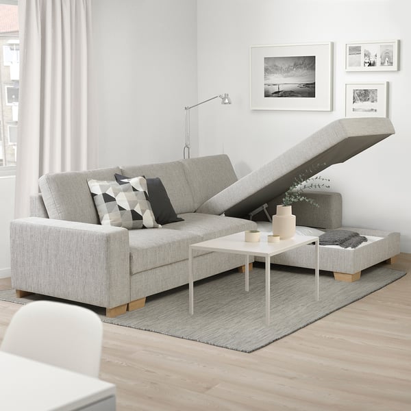 Divano beige moderno con chaise longue reclinabile, cuscini geometrici, tavolino e arte murale.
