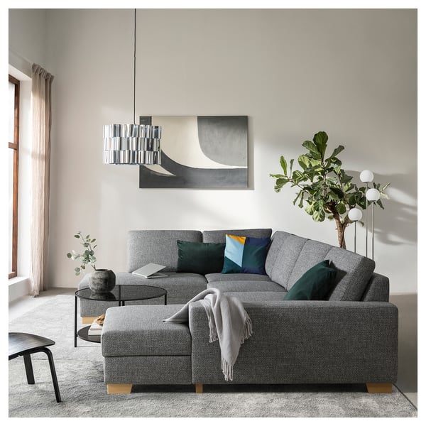 Soggiorno moderno con un grande divano componibile grigio SÖRVLEN, cuscini colorati, un tavolino in vetro e un'elegante lampada a sospensione.