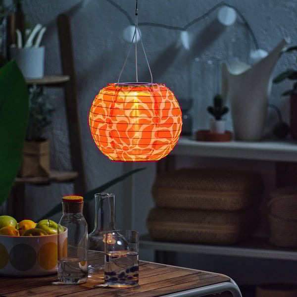 Ambiente esterno accogliente. La lanterna solare sospesa illumina un tavolo con bicchieri e frutta.