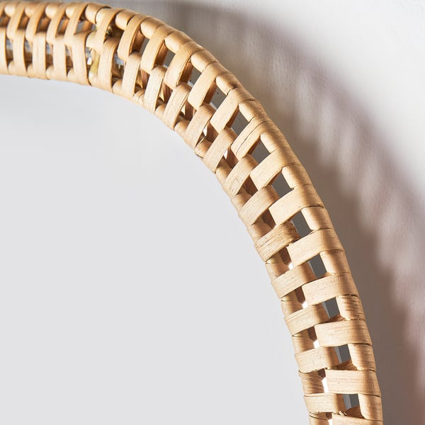 Bordo a specchio in rattan intrecciato, realizzato a mano con fibre naturali, che mostra un intricato motivo decorativo contro il muro.