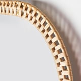 Bordo a specchio in rattan intrecciato, realizzato a mano con fibre naturali, che mostra un intricato motivo decorativo contro il muro.
