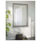 Uno specchio da parete con cornice vintage e pellicola di sicurezza, appoggiato a una parete accanto a una porta, che riflette una porta all'interno di un'abitazione.