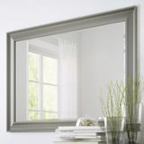 Grande specchio con opzioni di sospensione verticale e orizzontale, superficie riflettente, con pellicola di sicurezza. Mostrato sulla finestra riflettente a parete, accanto a piante e libri.