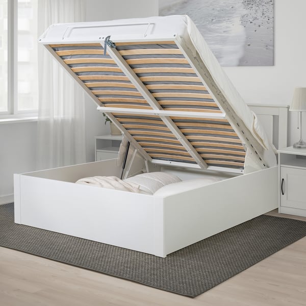 Pouf letto bianco con rete a doghe sollevata per mostrare lo spazio di archiviazione.