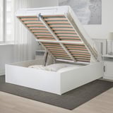 Pouf letto bianco con rete a doghe sollevata per mostrare lo spazio di archiviazione.