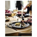 Tavolo da pranzo apparecchiato con posate scure, carciofo, limone, bicchiere da vino, candele.