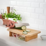 Persona che taglia il cetriolo su un tagliere di legno con fessure per catturare le fette.