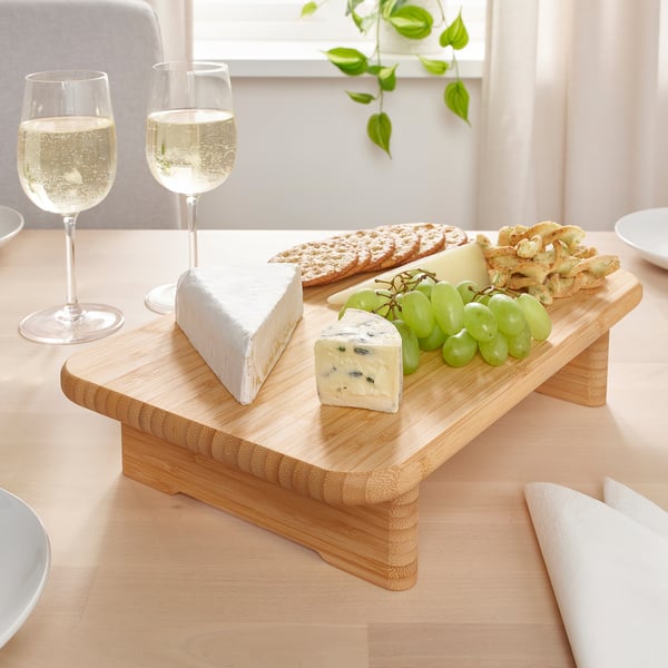 Tagliere in legno con formaggi, uva e cracker; un bicchiere di vino.