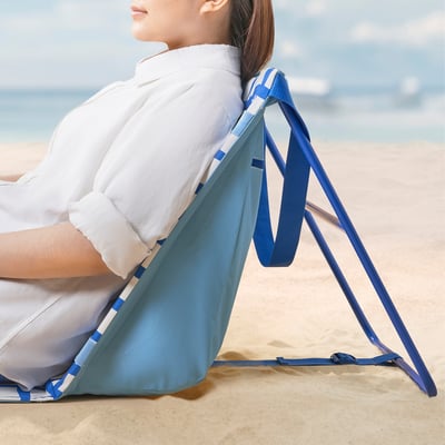La persona si rilassa sulla sedia da spiaggia blu regolabile STRANDÖN, mostrando la sua facilità di installazione e conservazione.