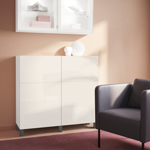 Mobile STUBBARP bianco con gambe grigio scuro, parete pesca, vasi, mobile vetrato, poltrona grigio scuro, tappeto bordeaux, stile minimalista.