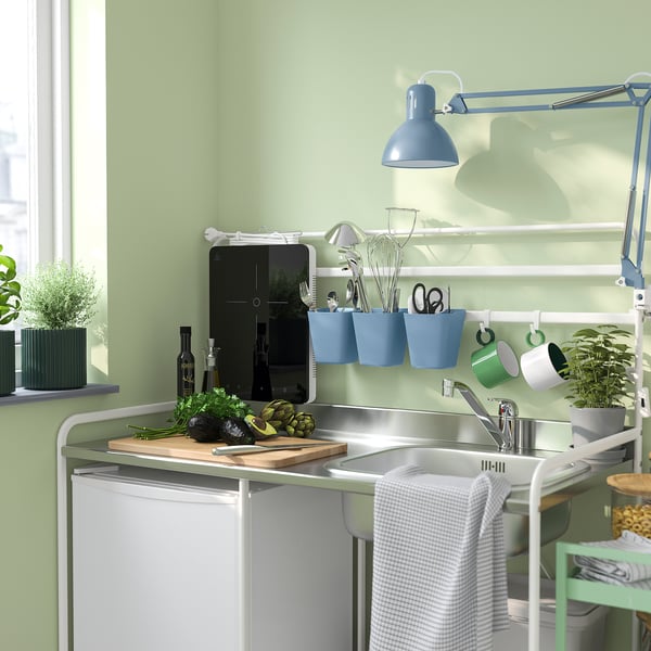 Piccolo organizer blu SUNNERSTA da appendere alla parete della cucina, con forbici, cucchiai e tazze. Parete verde e lavandino bianco.