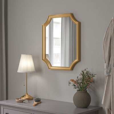 Specchio SVANSELE con cornice dorata sopra il comò grigio con lampada, vaso e oggetti personali.