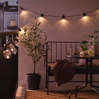 Accogliente balcone decorato con luci a stringa SVARTRÅ . Mobili in metallo nero, pianta in vaso e illuminazione calda creano un'atmosfera rilassante.