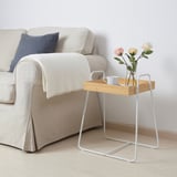 Tavolino in bambù bianco SVENARUM accanto al divano beige, con fiori e una tazza blu, che aggiunge un tocco chic minimalista.