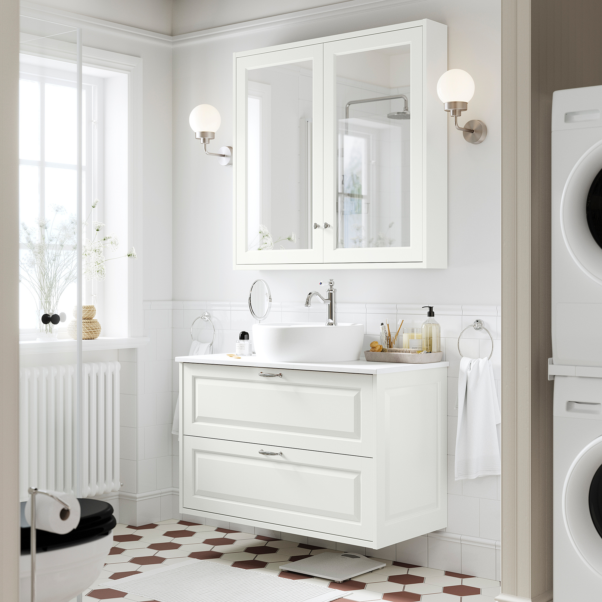 Moderno bagno bianco con lavabo TÄNNFORSEN, specchio, lampade, pavimento a motivi geometrici, lavatrice e lavabo rotondo.
