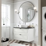 Bagno moderno bianco con mobile TÄNNFORSEN. Specchio rotondo, lavello a vaso, piastrelle geometriche per pavimenti, lavatrice bianca. Design elegante e spazioso.