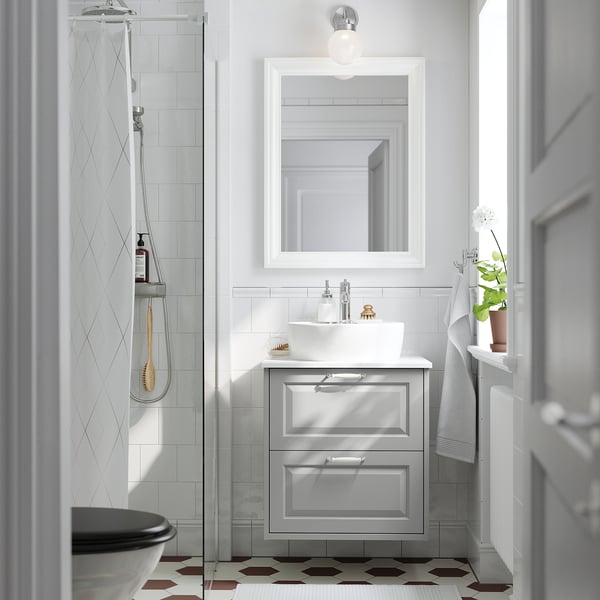 Bagno moderno con lavabo bianco TÄNNFORSEN, lavabo, specchio a parete, doccia in vetro, piastrelle a motivi geometrici e pianta in vaso.