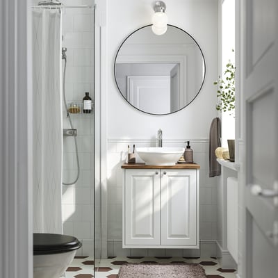 Bagno moderno e minimalista: lavabo bianco TÄNNFORSEN, specchio rotondo, doccia con porta in vetro, piastrelle esagonali scure.