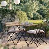 Set da giardino esterno con tavolo e sedie in legno marrone, sedute imbottite, immerso nel verde.