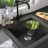 Lavello da fattoria nero con cestello in acciaio inox riempito di sedano. Cucina moderna con rubinetto nero e vari accessori.